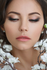 Beauty portrait of a beautiful girl with an elegant wedding makeup with blossoming sakura.