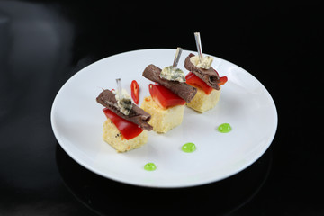 sliced meat, rolled into a roll, canapes with blue cheese and red pepper, on a skewer, close-up