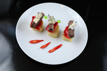 sliced meat, rolled into a roll, canapes with blue cheese and red pepper, on a skewer, close-up