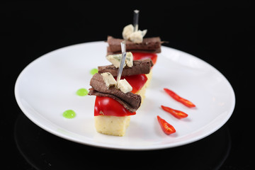 sliced meat, rolled into a roll, canapes with blue cheese and red pepper, on a skewer, close-up