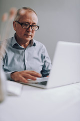 Good-looking senior man in glasses using modern laptop