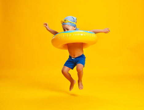 happy child boy in swimsuit with swimming ring donut on colored yellow background.
