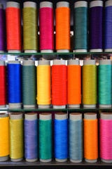 Three rows of vertically placed technical thread bobbins at the exhibition. Polypropylene multifilament yarns. Set of sewing thread coils, miscellaneous colours.