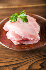 Chicken fillet with a sprig of parsley on a wooden plate on a textural table. Raw turkey meat close up and copy space.