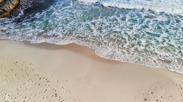 aerial drone shot of a rocky coastline in Majorca with waves crashing onto the rocks and sandy beach of the Mediterranean