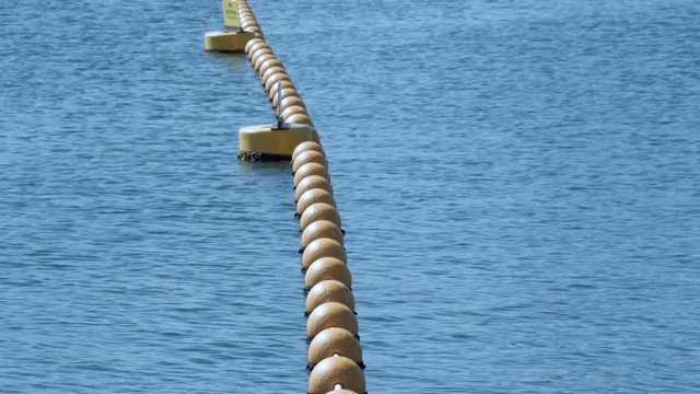 Endless sea view with a chain of yellow coloured buoys. A barrier chain on the coastline. PAN UP SHOT.