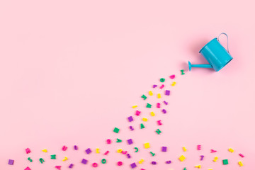 Bright multicolored Multicolored plastic numbers and letters flow from watering can on pink background. Learning, education, math, reading concept