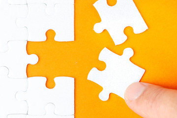 Hand holding piece of white puzzle on orange background