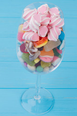 Goblet glass filled with colorful candies. Wine glass with assorted candies, sweets and marshmallows. Blue wooden background.