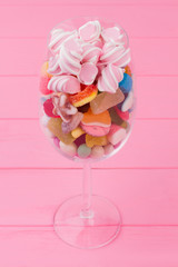 Various candies in wine glass. Transparent glass full of colorful candies and sweets on pink background.