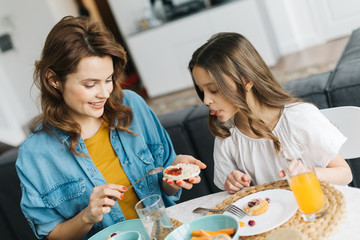 Woman putting jam on crisp bread and daughter showing her tongue