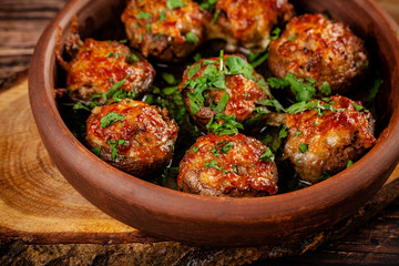 The concept of Georgian cuisine. Baked mushrooms champignons with meat and cilantro. Serving dishes in a restaurant in a plate made of red clay. On a wooden background. copy space