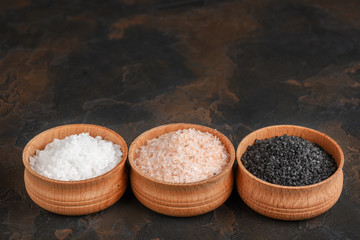 White (sea), pink (himalayan) and black salts in wooden bowls on dark background
