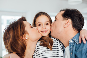 Happy parents kissing their daughter on cheek