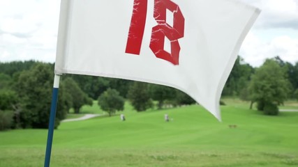 Golf flag waving on a bright sunny windy day with cloudy sky. White Flag Hole Number 18. Close Up Summer landscape, cloudscape