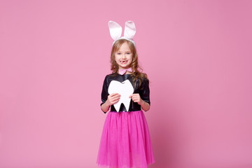 Happy girl in the form of an Easter Bunny with the layout of the human tooth. Milk teeth are changed to permanent. Concept of medicine. Dentist day. Selective focus.