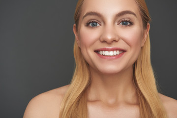 Fototapeta premium Portrait of positive woman smiling while standing against the grey background