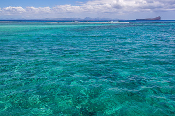 Bright sunlight passes through clear turquoise water in lagoon with  near tropical island Mauritius