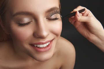Cheerful woman smiling while beautician applying false eyelashes