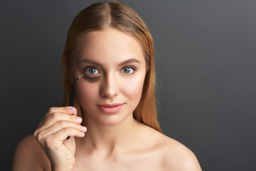 Joyful woman putting false eyelashes on her face and smiling