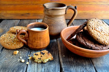 Obraz na płótnie Canvas Oatmeal cookies in a ceramic rustic plate, milk in a ceramic mug, napkin, honey on a rustic wooden table.