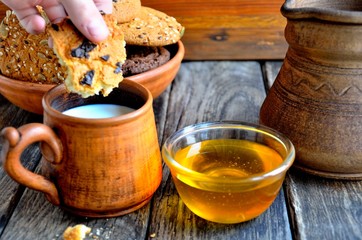 Oatmeal cookies in a ceramic rustic plate, milk in a ceramic mug, napkin, honey on a rustic wooden table.