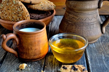 Fototapeta na wymiar Oatmeal cookies in a ceramic rustic plate, milk in a ceramic mug, napkin, honey on a rustic wooden table.