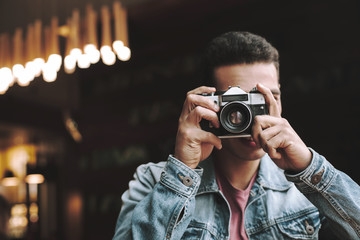 Young man in denim jacket taking picture with retro camera