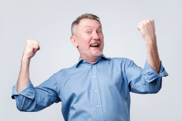 Fototapeta premium Happy senior strong man, raising clenched fists in hooray gesture, triumphing