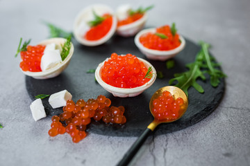 Red caviar on black plate with spoon and creamy cheese. Food photo concept