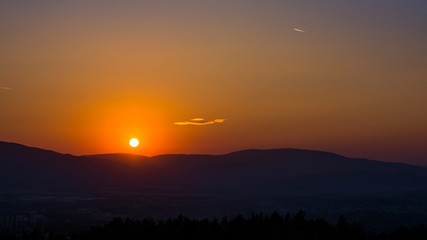 Landscape with the sunset. Clear orange sky with little cloud and dark landscape.