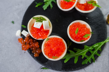 Red caviar on black plate with spoon and creamy cheese. Food photo concept