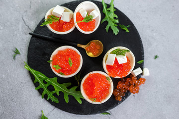 Red caviar on black plate with spoon and creamy cheese. Food photo concept