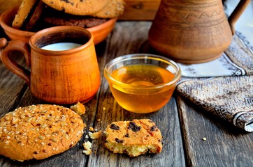 Oatmeal cookies in a ceramic rustic plate, milk in a ceramic mug, napkin, honey on a rustic wooden table.