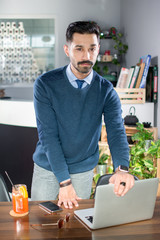 Portrait of handsome young man in smart casual wear with hands over the working table and laptop in a office