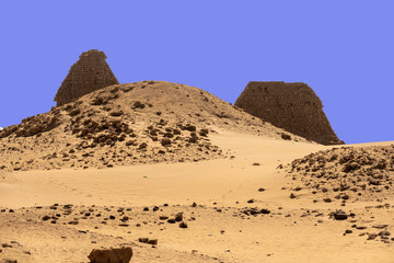 A pyramid destroyed beyond recognition in the foreground, two restored pyramids in the background in the desert of Sudan.