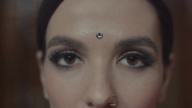 Close-up of attractive indian woman's face with oriental makeup, charming dark eyes, long black eyelashes and bindi point on forehead. Young woman shyly looking down and then opening eyes wide.