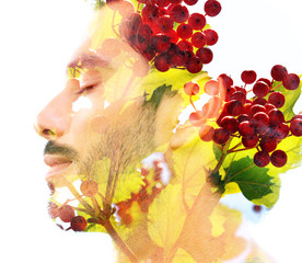 Double exposure of a young handsome man’s portrait blended with bright green leaves with red fruits, showing the perfect beauty of nature's creation
