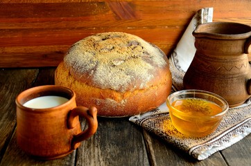 Rustic bread, ceramic mug with milk, honey, napkin on a wooden table.