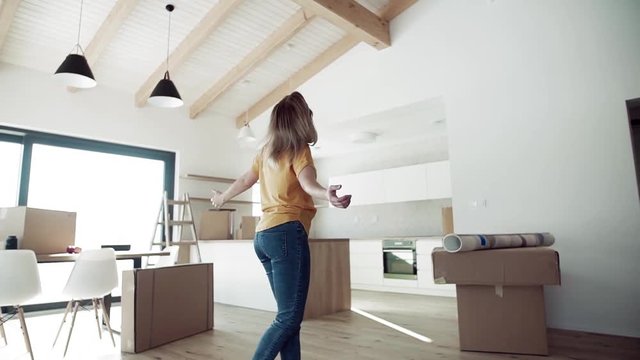 A joyful young woman moving in new home, expressing excitement. Slow motion.