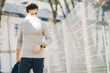 stylish man walking through the city smoking an e-cigarette