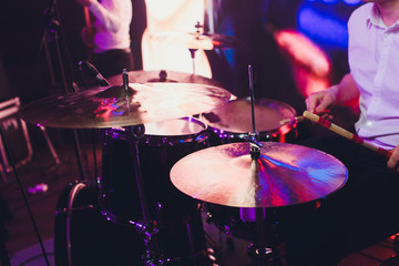 Drummer with a drumsticks in his hands playing on drum set on stage on the black background.