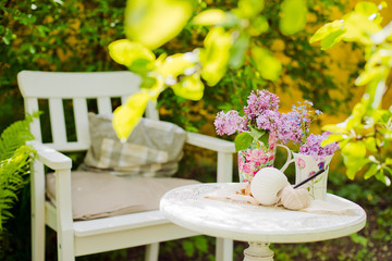 White wooden chair table with a bouquet of lilacs spring garden. needlework, knitting Recreation area shade of trees own garden. Relax in nature. Clean air, peace for creativity and inspiration.
