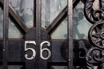 House number 56 with the fifty six in silver numerals with the door locked behind metal bars - a locked and guarded house door