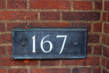 House number one hundred sixty seven in white lettering on old black metal. The 167 is clearly visible on a brick wall