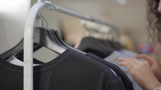 Woman is looking for t-shirt on rack in clothing store, close-up of her hands