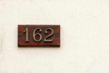 House number one hundred sixty two on an off white wall with the 162 in bronze lettering on a natural wooden panel