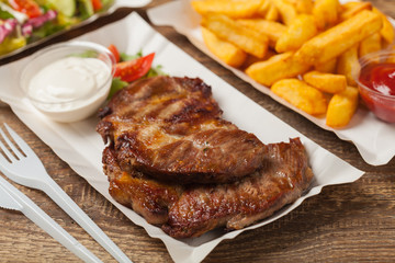 Grilled pork neck served on paper trays.