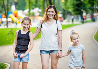 Smiling mom with little daughters walking by holding hands