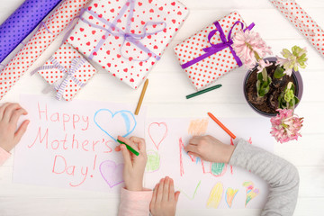 Little girl drawing happy mother's day greeting card with presents on the table. Mothers day background